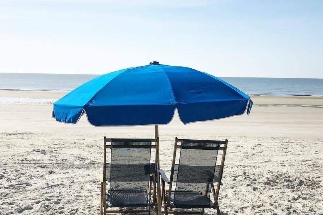 Two beach chairs under a blue umbrella on the sand